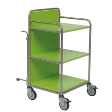 A Novocal station trolley made of stainless steel with fully welded round tube connections is shown empty on a white background. It features three shelves, metal rails, and four wheels - one of which has a brake lever.