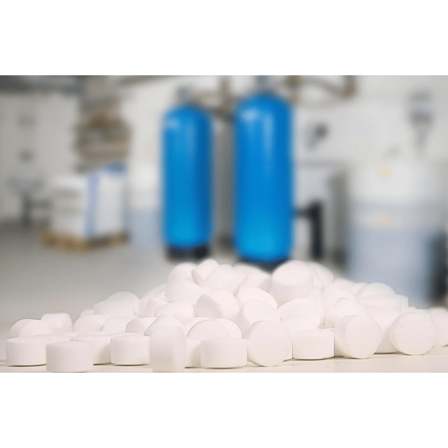 In the foreground, there is a stack of AXAL PRO TABS regenerating salt - special salt for water softening by K+S Minerals and Agriculture GmbH, with two large blue tanks visible in the blurred background, presumably belonging to a water softening system.