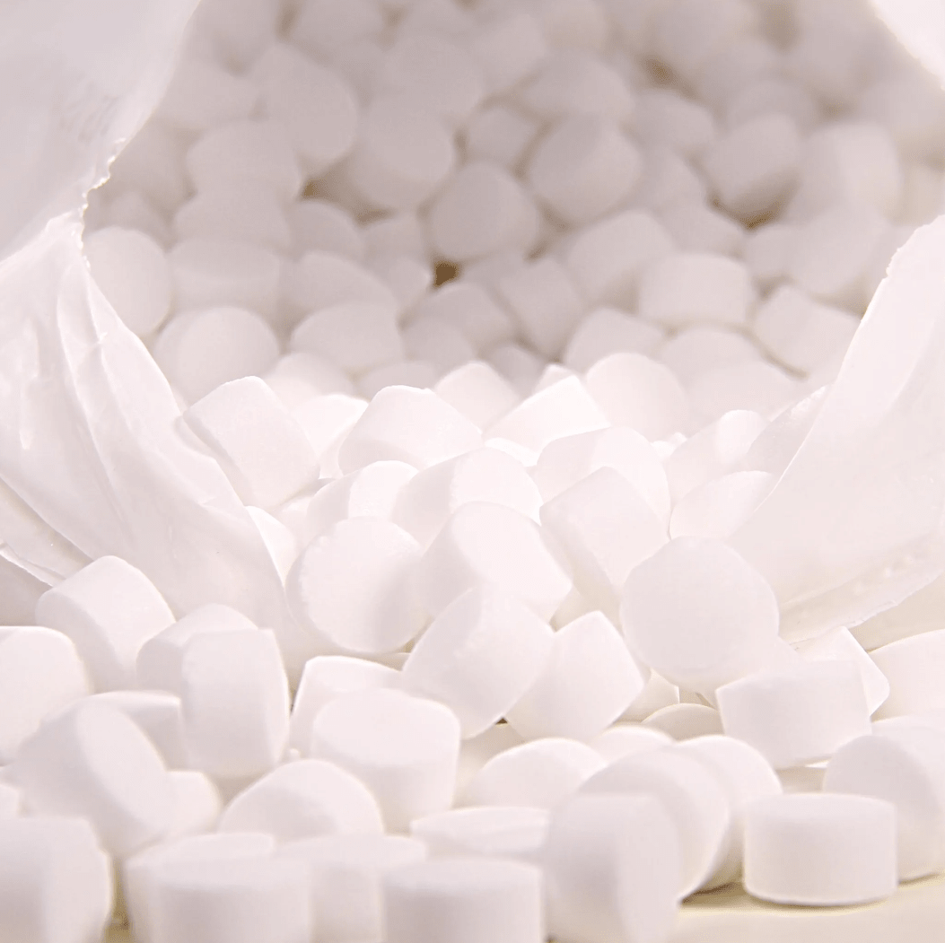 Numerous white, round tablets fall from an opened white bag of AXAL PRO TABS regenerating salt by K+S Minerals and Agriculture GmbH onto a surface, perfect for water softening.