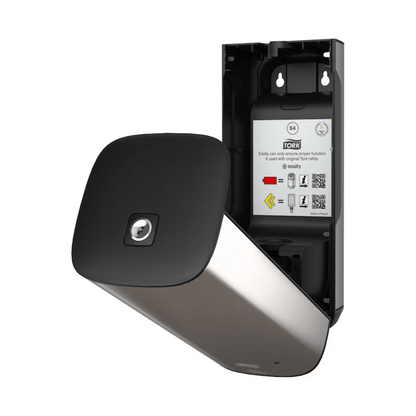 The Tork 460009 Skincare Dispenser from TORK – Essity Professional Hygiene Germany GmbH is openly presented and features a stylish, modern design with a metallic surface and a black front panel. Inside, operating instructions and QR codes are visible. This wall-mounted stainless steel dispenser is designed for efficient towel use and features innovative Intuition Sensor technology.