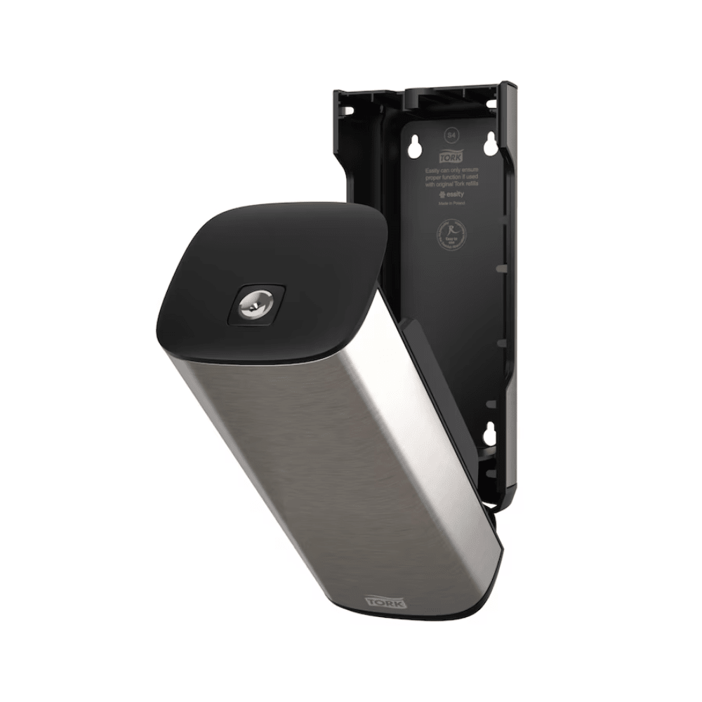 A Tork 460010 dispenser for soap and hand sanitizers in stainless steel and black from Essity Professional Hygiene Germany GmbH for wall mounting with an open front panel that reveals the interior compartment. This modern design also features a partially detached plate that exposes the interior bracket and screw positions.