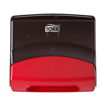 A Tork 654008 single towel dispenser Performance W4 paper towel dispenser is mounted on a white wall. The upper part is black and the lower part is red. The Tork logo, associated with Essity Professional Hygiene Germany GmbH, appears in white on the black area.