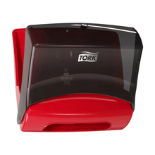 A Tork 654008 single towel dispenser Performance W4 from Essity Professional Hygiene Germany GmbH is mounted on the wall in red and black colors. Its transparent black cover provides a good view of the wipe roll inside, making it ideal for professional cleaning.
