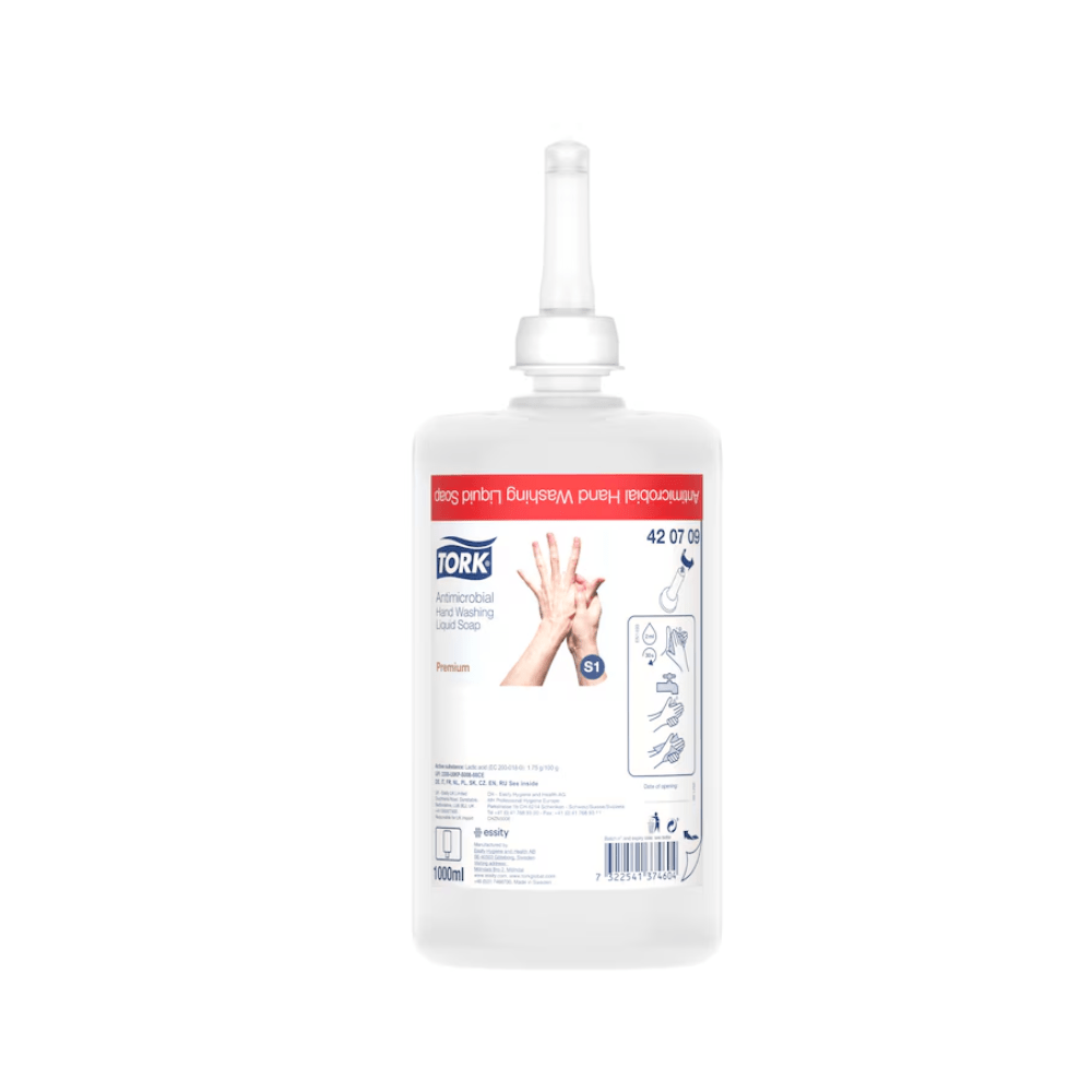 Pictured is a Tork liquid soap for hand decontamination refill bottle with a nozzle. The label shows usage instructions, the brand name TORK – Essity Professional Hygiene Germany GmbH, and product details. The transparent bottle reveals the liquid inside, emphasizing its use in food processing. The label is predominantly in red and white colors.