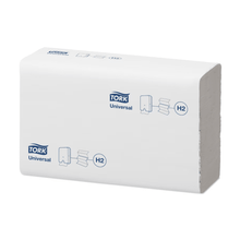 A stack of Tork Xpress® 471093 Universal H2 Multifold Towels is seen against a plain white background. The packaging, adorned with the blue TORK logo of Essity Professional Hygiene Germany GmbH, displays symbols indicating the use of multifold towels. The rectangular stack has a visible open edge, highlighting its practical design.