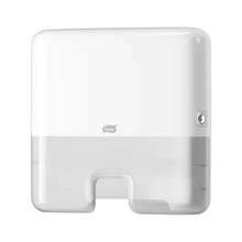 A Tork Xpress® 552100 Mini Dispenser for Multifold Hand Towels Elevation H2, manufactured by TORK – Essity Professional Hygiene Germany GmbH, is wall-mounted. It features a simple rectangular design with rounded edges, a visible lock on the right side, and an opening at the bottom for single sheet dispensing of multifold towels.