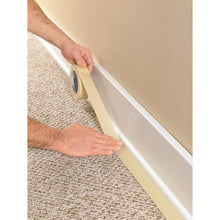 A person uses the Scotch® Classic masking tape, 24 mm x 50 m (70% PEFC) from 3M Deutschland GmbH, to tape off the baseboard where the carpet meets the wall, to protect the trim during painting and renovation work.