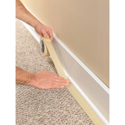 A person uses the Scotch® Classic masking tape, 24 mm x 50 m (70% PEFC) from 3M Deutschland GmbH, to tape off the baseboard where the carpet meets the wall, to protect the trim during painting and renovation work.