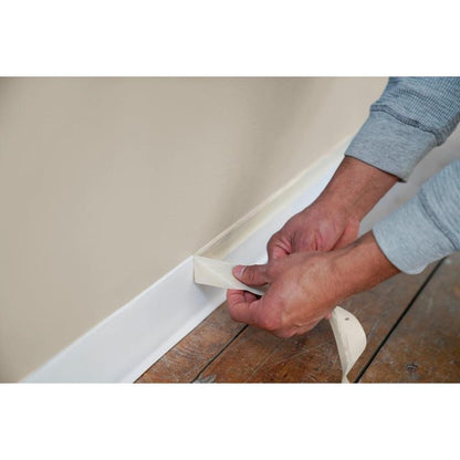 During painting and renovation work, a strip of Scotch® Classic masking tape (24 mm x 50 m, 1 roll/pack, 70% PEFC) from 3M Deutschland GmbH is peeled off the top of a white baseboard along a beige wall with a wooden floor.