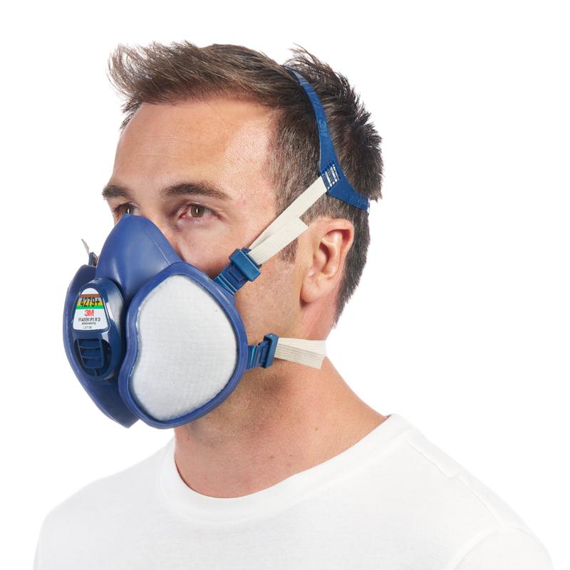 A man with short brown hair and a white shirt is seen in profile. He wears the 3M™ respirator with integrated filters from 3M Deutschland GmbH, featuring a blue design and adjustable headbands.