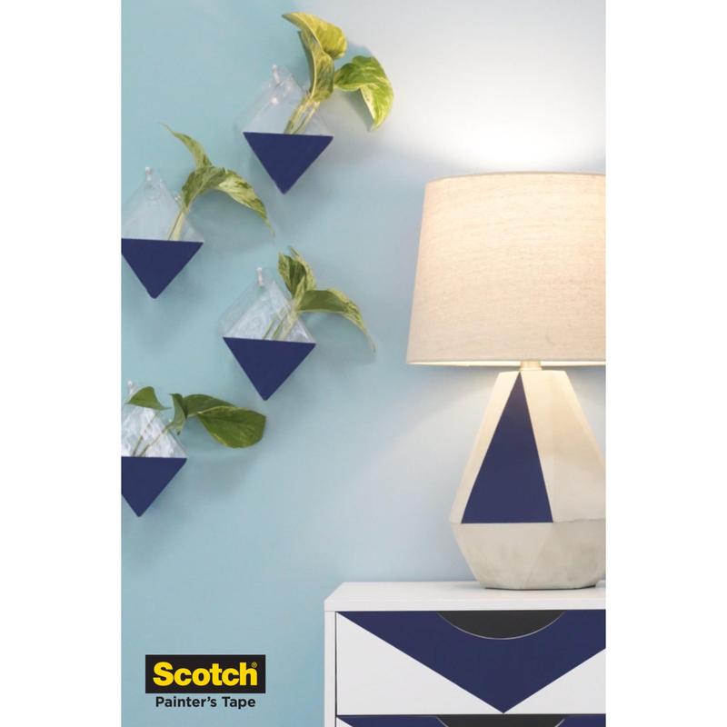 A blue-white geometric dresser and a lamp stand in front of a blue wall with triangular planters, all protected with Scotch® Painter's Tape for delicate surfaces (36 mm x 41 m, 1 roll) from 3M Deutschland GmbH. The logo appears at the bottom left.