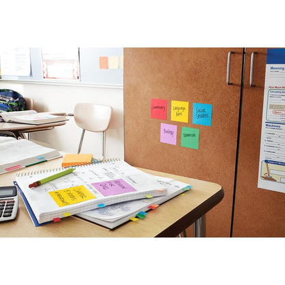 A classroom with open notebooks, a calculator, and papers on a desk. 3M Post-it® Super Sticky Z-Notes (Boost Collection, 76x76mm, PEFC) are used to label school subjects on a cabinet. Empty chairs and posters fill the background.
