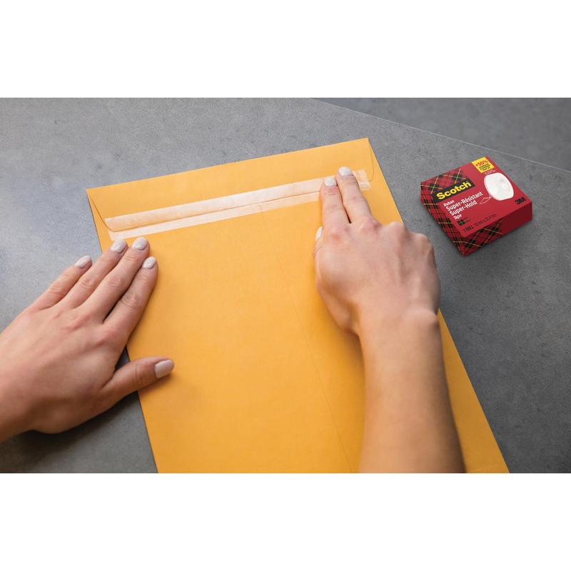 A person seals a large brown envelope with Scotch® Super-Hold Secure Tape, 1 roll, 19 mm x 25.4 m from 3M Deutschland GmbH on a gray surface. The tape box is nearby and ensures a strong and transparent bond for secure mailing.