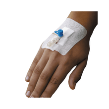 A hand with an intravenous needle inserted into the tip, secured with a Holthaus Ypsipor cannula dressing 9 x 6 cm from Holthaus Medical GmbH & Co. KG. A transparent tube connects the needle to a blue cap on the medical device. The skin is visible around the precise fixation of the cannula.